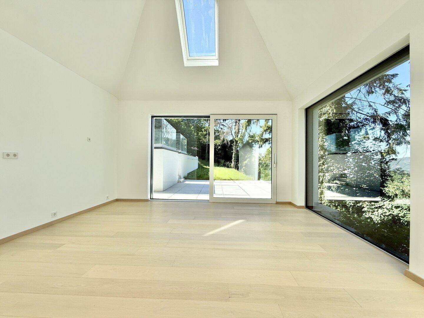 Heller Raum mit Holzboden, hohen Decken und großen Fenstern mit Zugang zum Außenbereich.