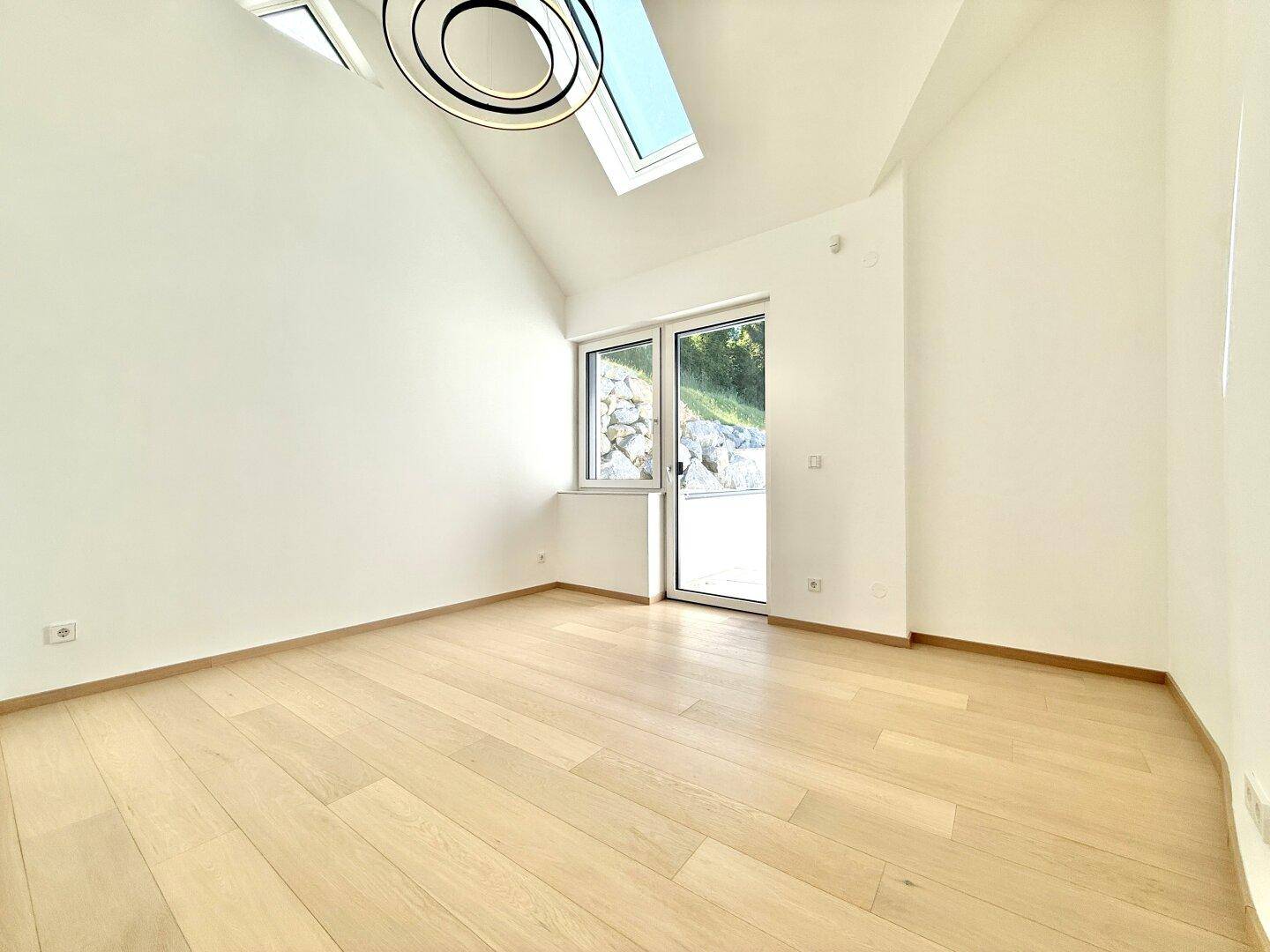 Heller Raum mit Holzboden, Dachfenster und Zugang zu einem kleinen Außenbereich.