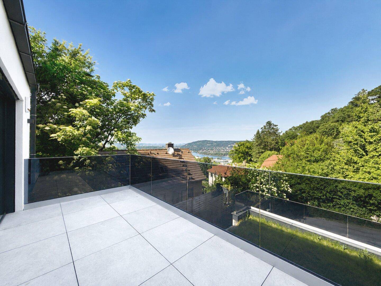 Balkon mit Glasbrüstung und weitem Blick über die Landschaft und den See.
