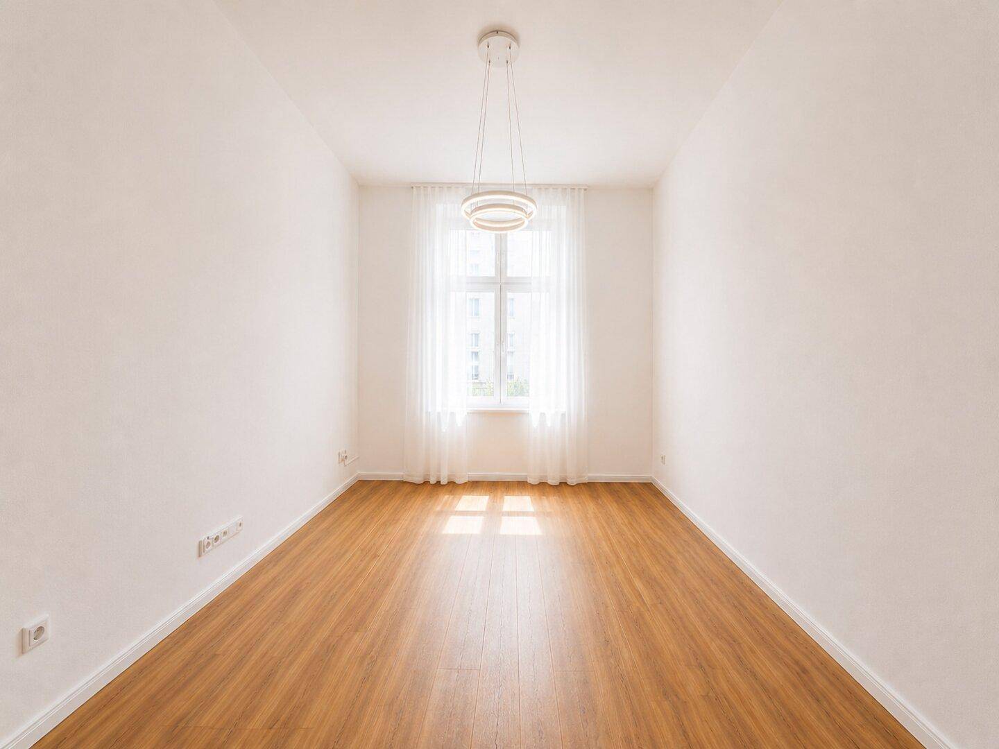 Leerer, heller Raum mit Holzboden und einem Fenster, ideal für ein Büro oder Gästezimmer.