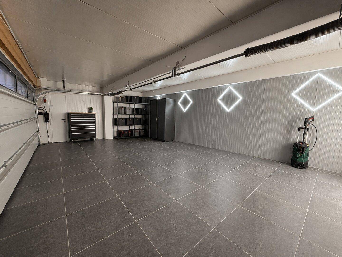 Geräumige Garage mit Fliesenboden, viel Stauraum und modernen Lichtelementen an der Wand.