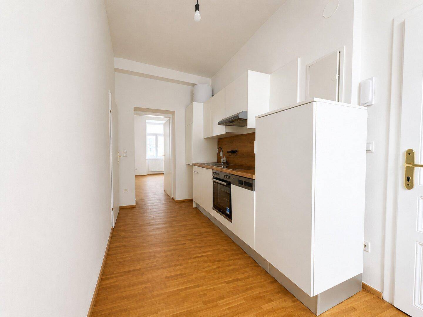 Funktionale, kompakte Küche mit weißen Schränken und Holzboden, offen zum angrenzenden Bereich.