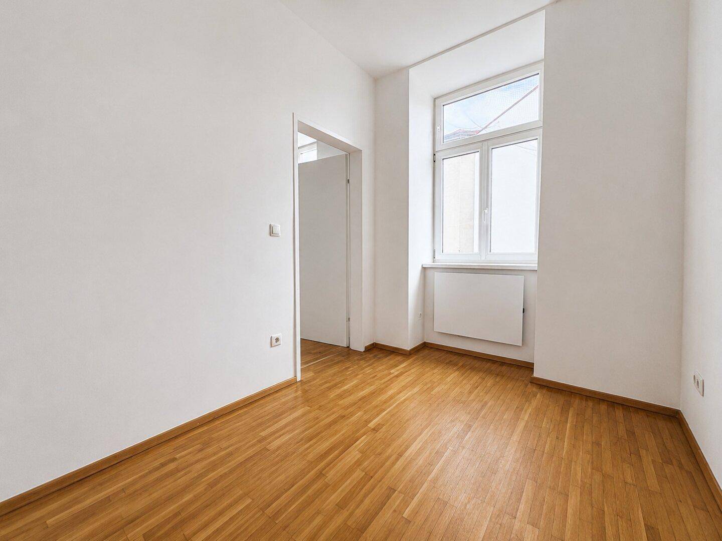 Kleineres, helles Zimmer mit Holzboden und einem Fenster, ideal als Schlaf- oder Arbeitszimmer.
