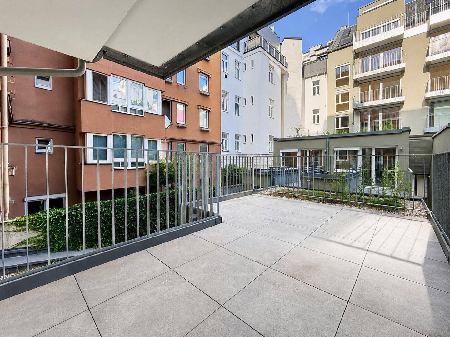 Geräumige, geflieste Terrasse mit stabilem Metallgeländer und Blick auf die angrenzenden Gebäude.