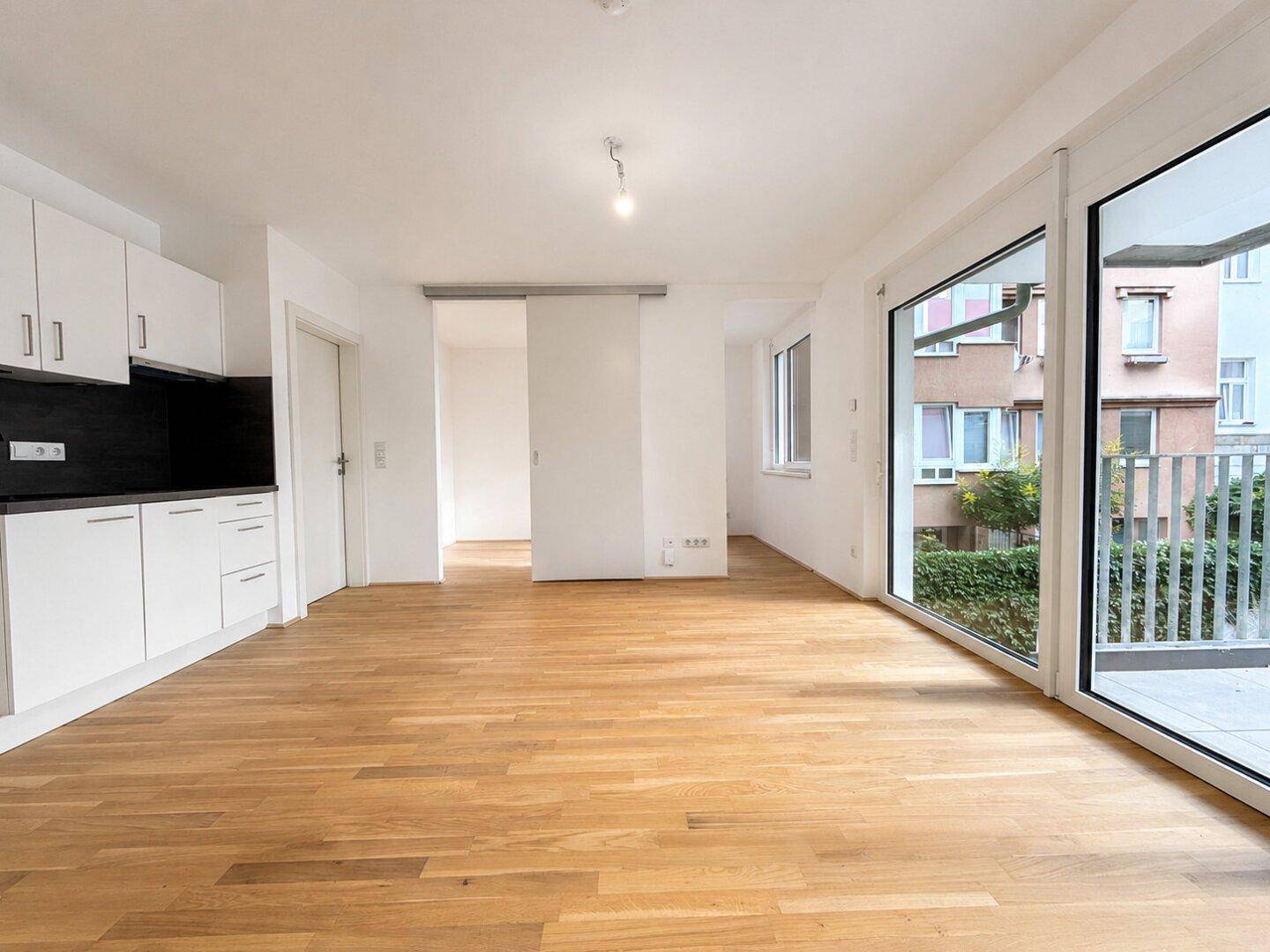 Heller Wohnbereich mit Holzboden, integrierter Küchenzeile und direktem Zugang zur Terrasse.