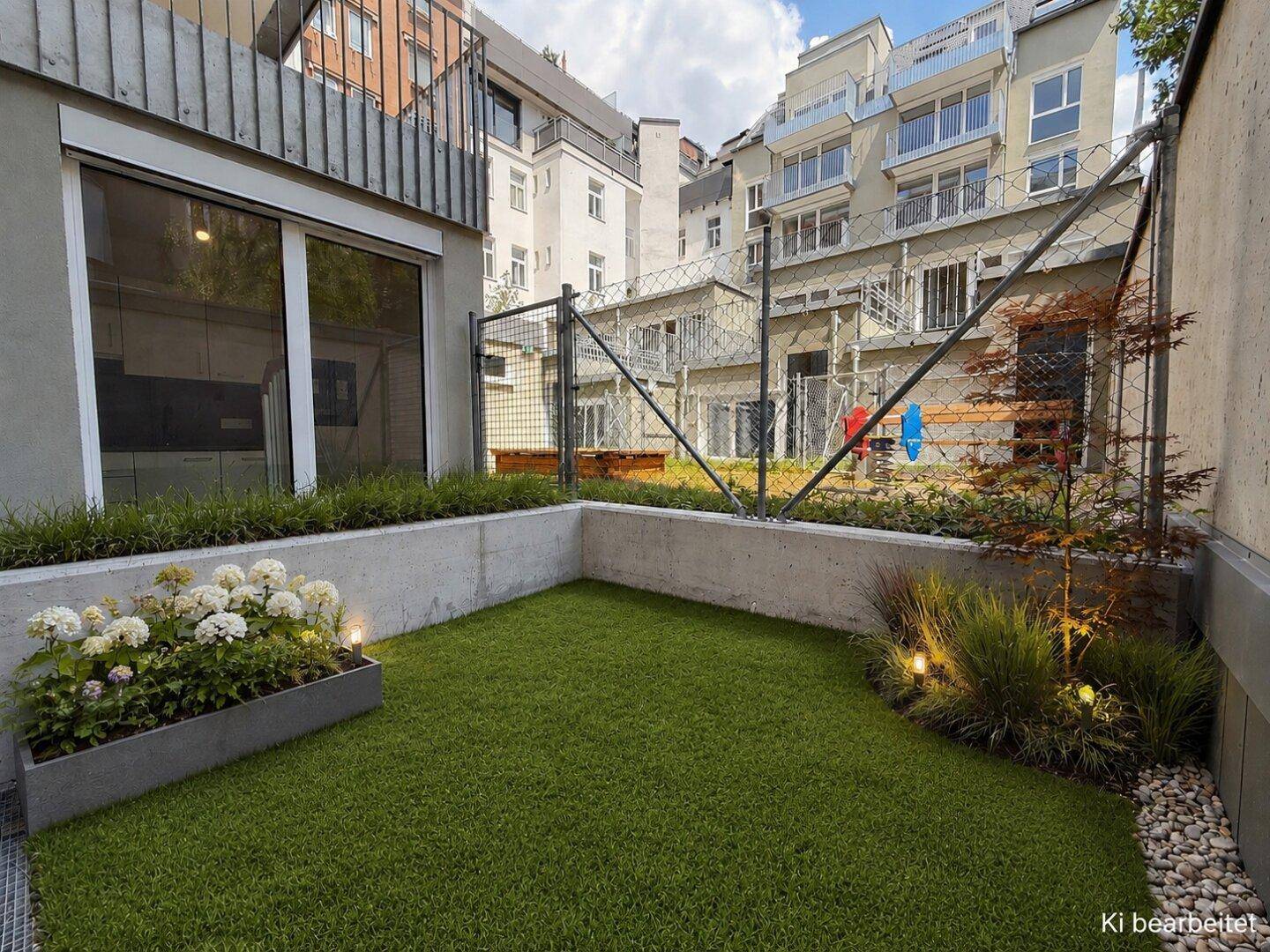 Kleiner, gepflegter Gartenbereich mit Rasenfläche, Blumenbeet und Blick auf umliegende Gebäude.