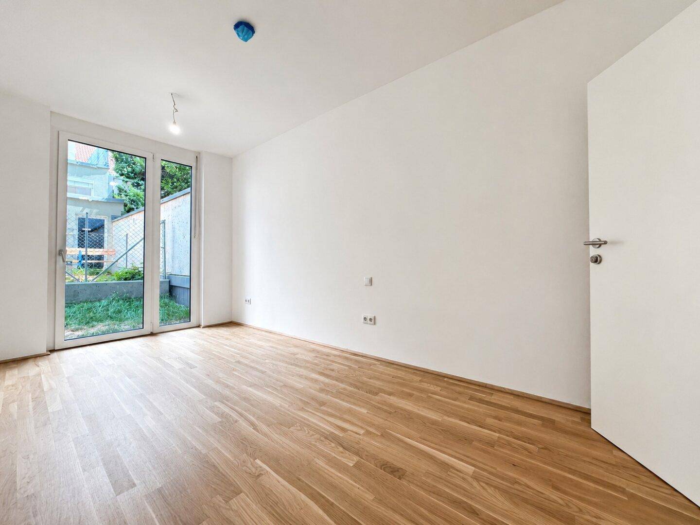 Leeres Schlafzimmer mit Holzboden und großer Fenstertür zum Außenbereich.