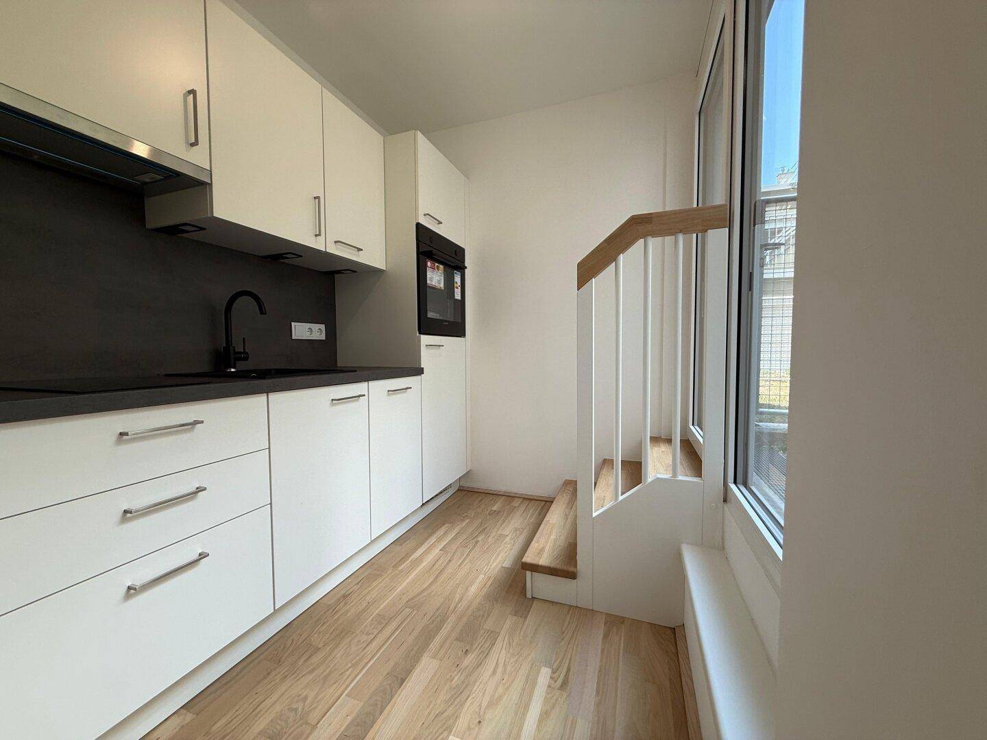 Moderne Einbauküche mit weißen Schränken, dunkler Arbeitsplatte und integriertem Backofen.
