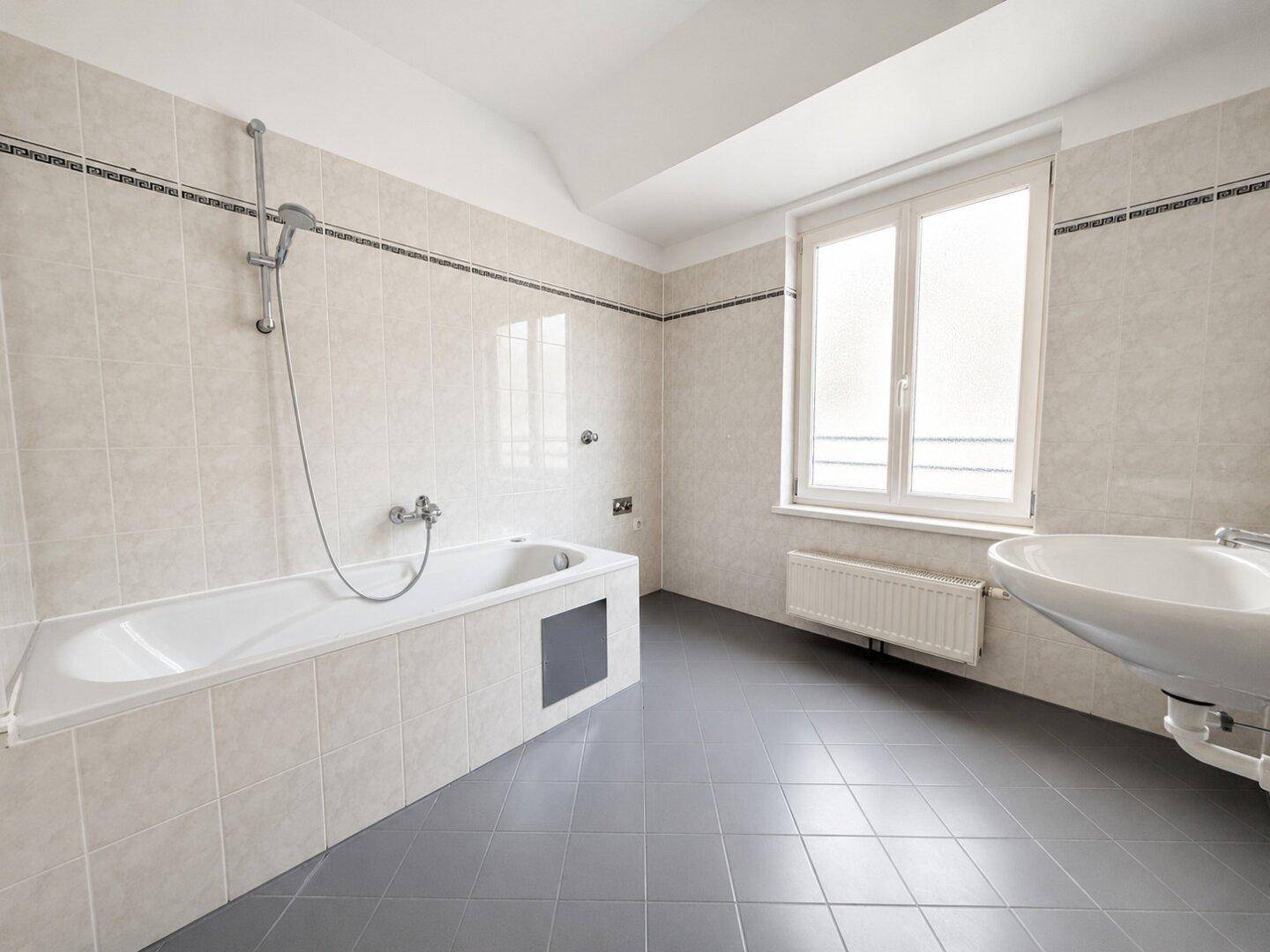 Geräumiges Badezimmer mit Badewanne, Waschbecken und Fenster.