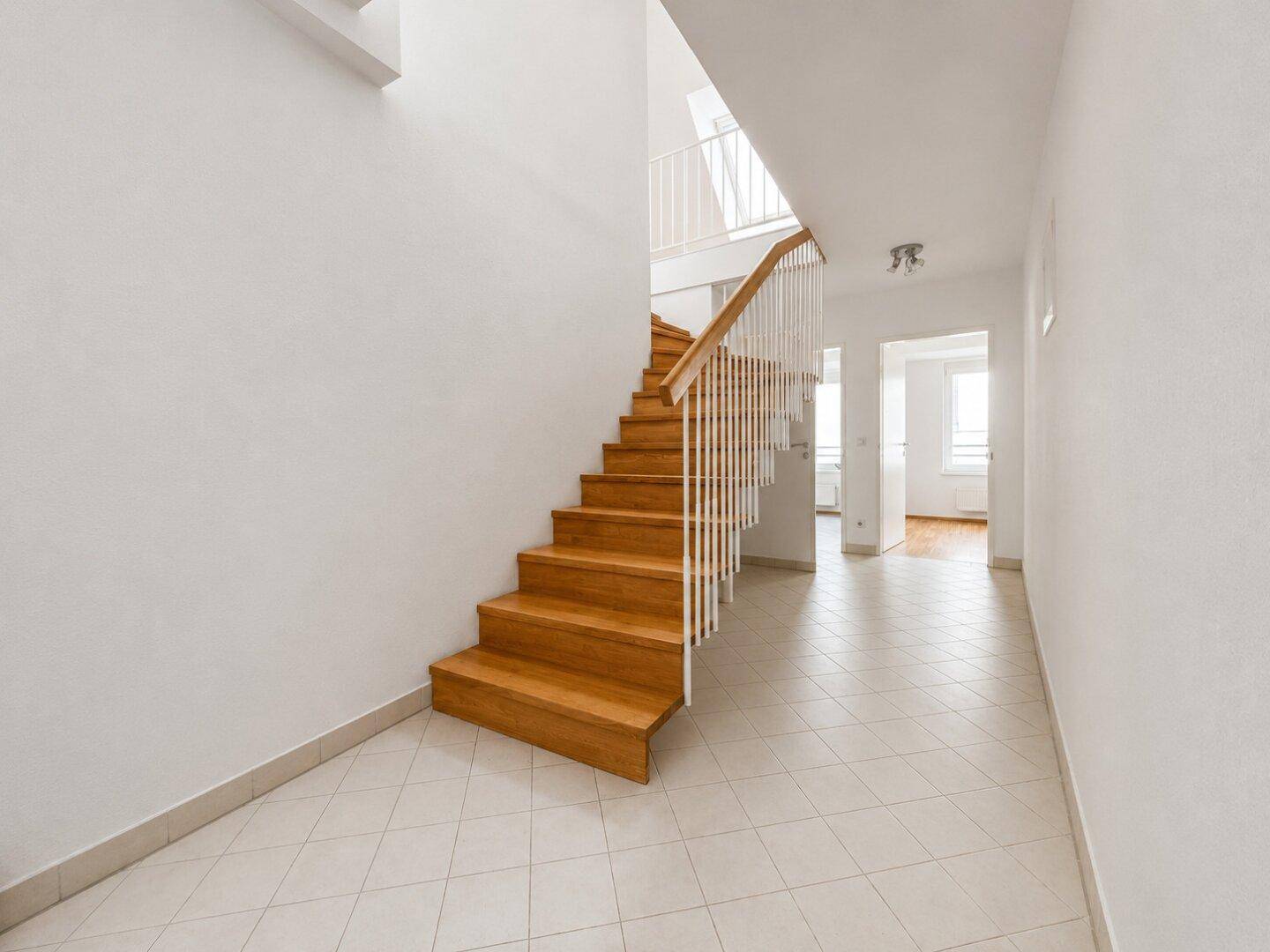 Heller Flur mit Holztreppe und Fliesenboden, der die Etagen verbindet.