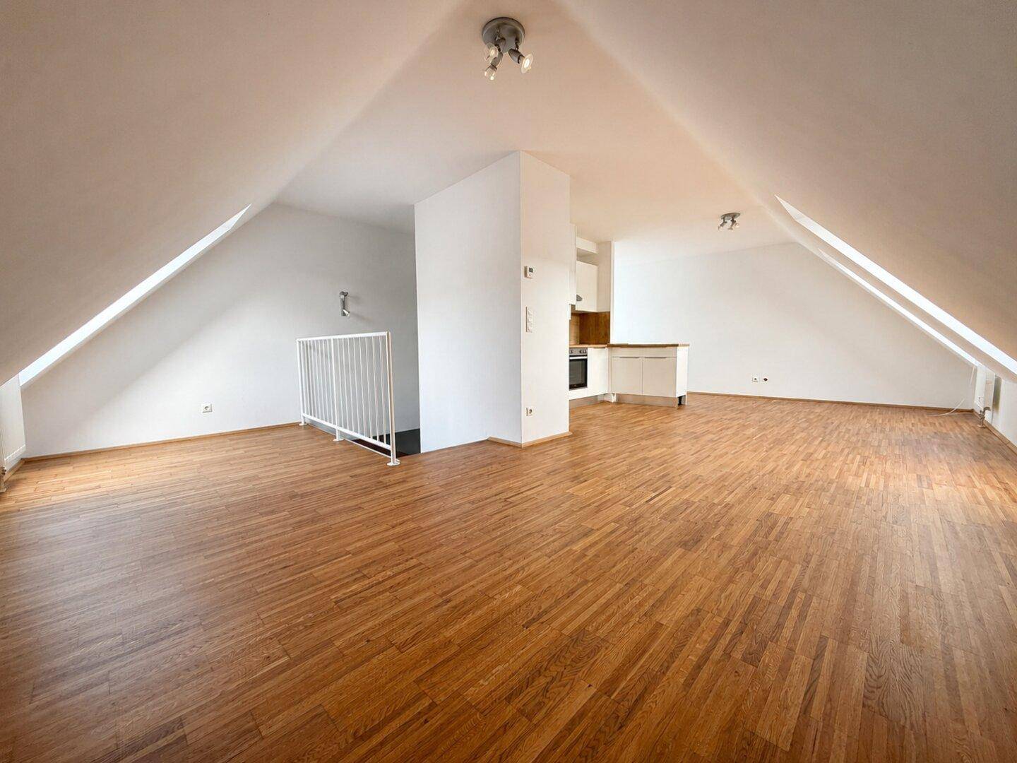 Geräumiger, leerer Raum im Dachgeschoss mit schrägen Wänden und Holzboden.