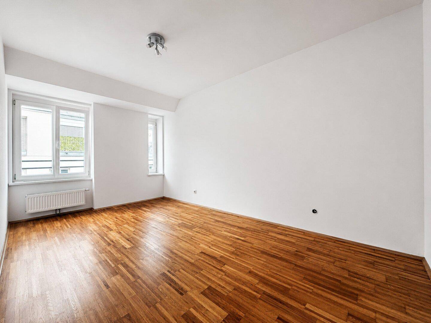 Leeres Zimmer mit Holzboden und großen Fenstern, bereit zur individuellen Gestaltung.