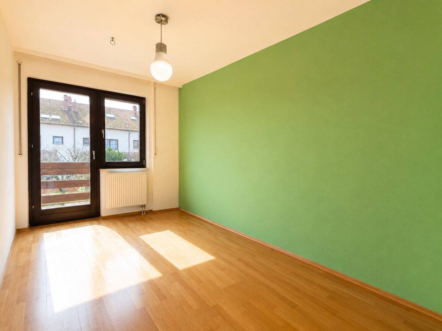 Schlafzimmer mit Parkettboden, grüner Akzentwand und Zugang zu einem französischen Balkon.