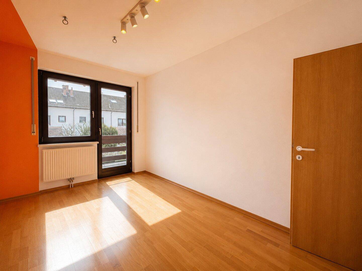 Schlafzimmer mit Parkettboden, orangefarbener Wand und Zugang zu einem französischen Balkon.