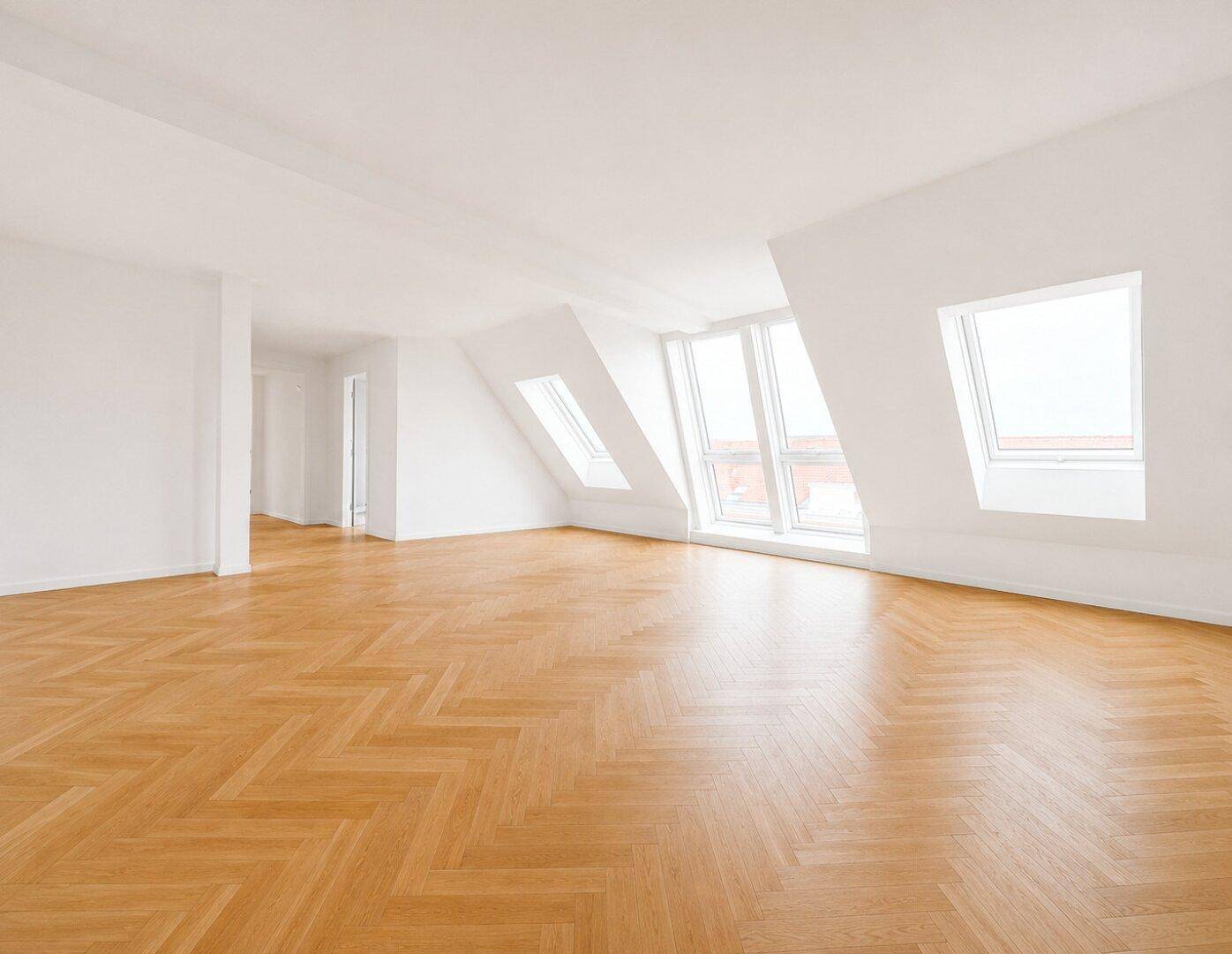 Geräumiger, unmöblierter Raum mit hellem Fischgrätparkett und großen Dachfenstern.