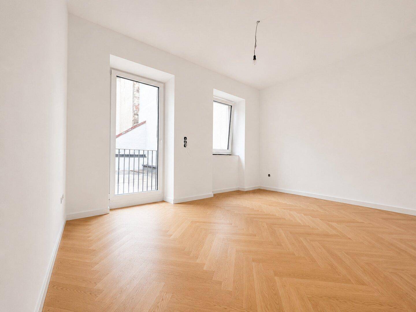 Leeres Schlafzimmer mit hellem Fischgrätparkett und Zugang zu einem französischen Balkon.