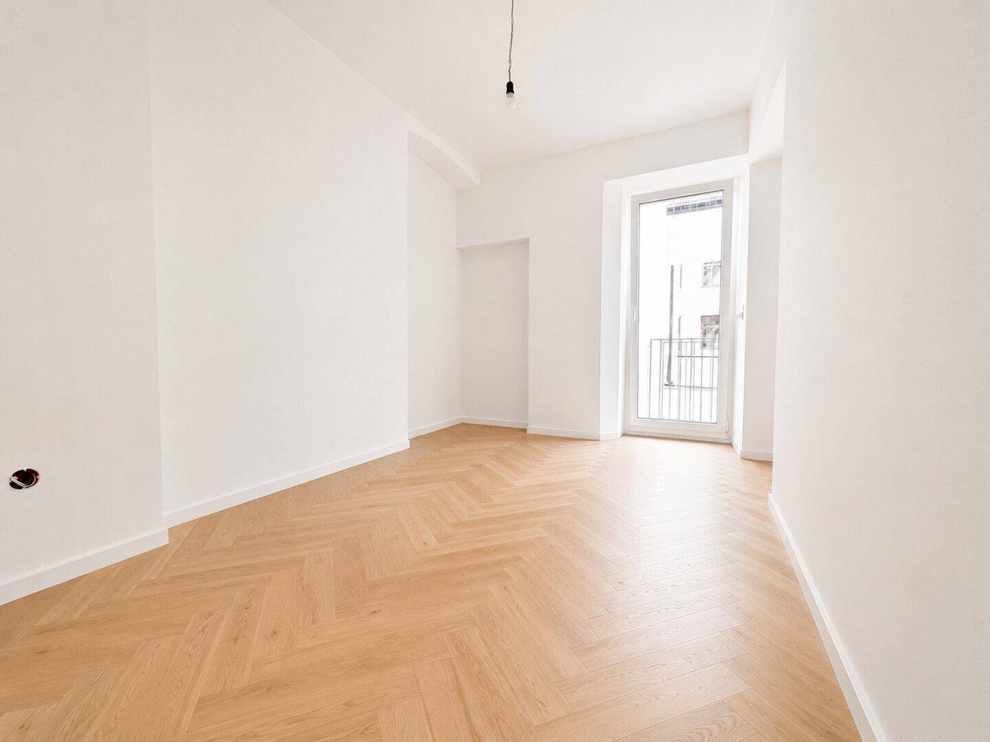 Kleineres, leeres Zimmer mit Fischgrätparkett und Zugang zu einem französischen Balkon.