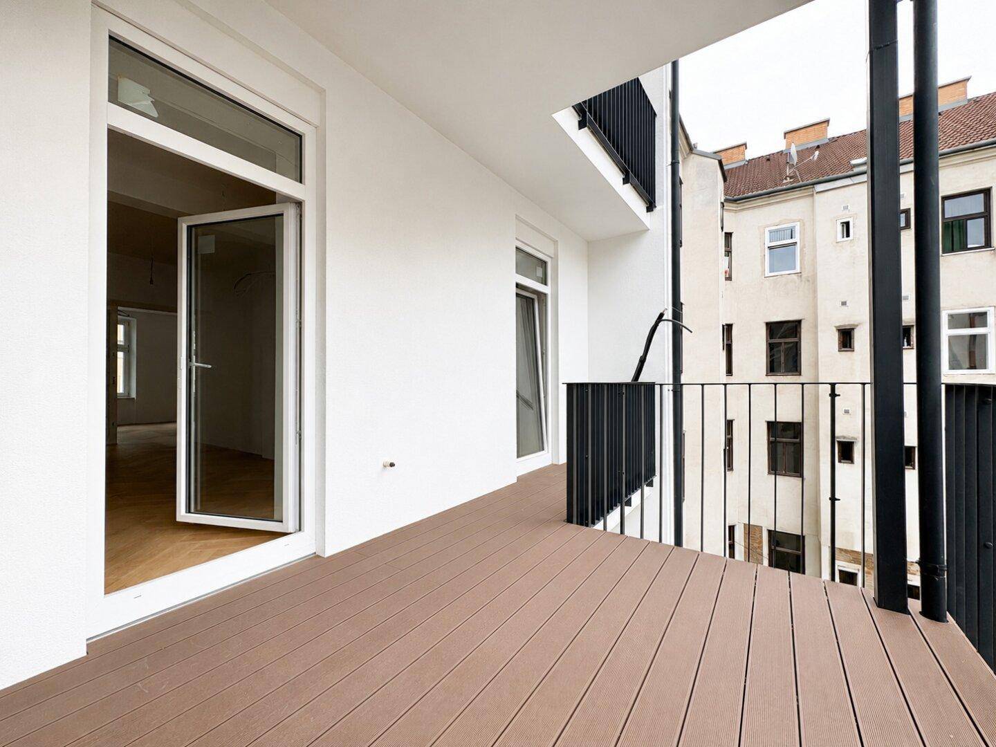 Geräumiger Balkon mit Holzboden und schwarzem Geländer, bietet Platz für Außenmöbel.