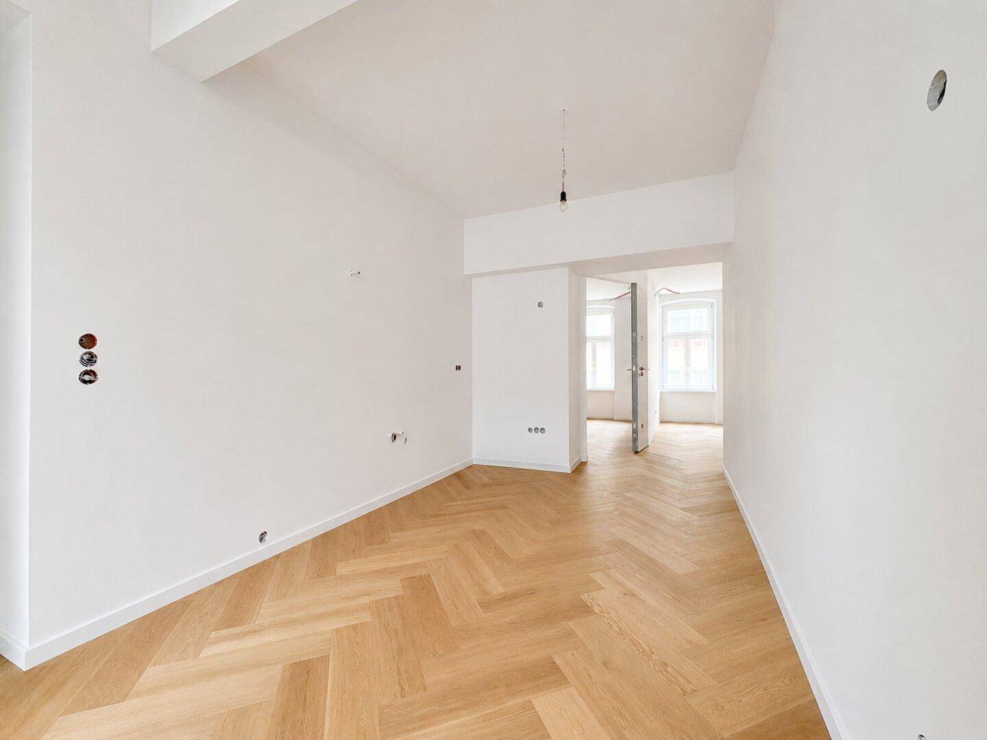 Leerer Raum mit Fischgrätparkett und Blick in angrenzende Zimmer, ideal für individuelle Nutzung.