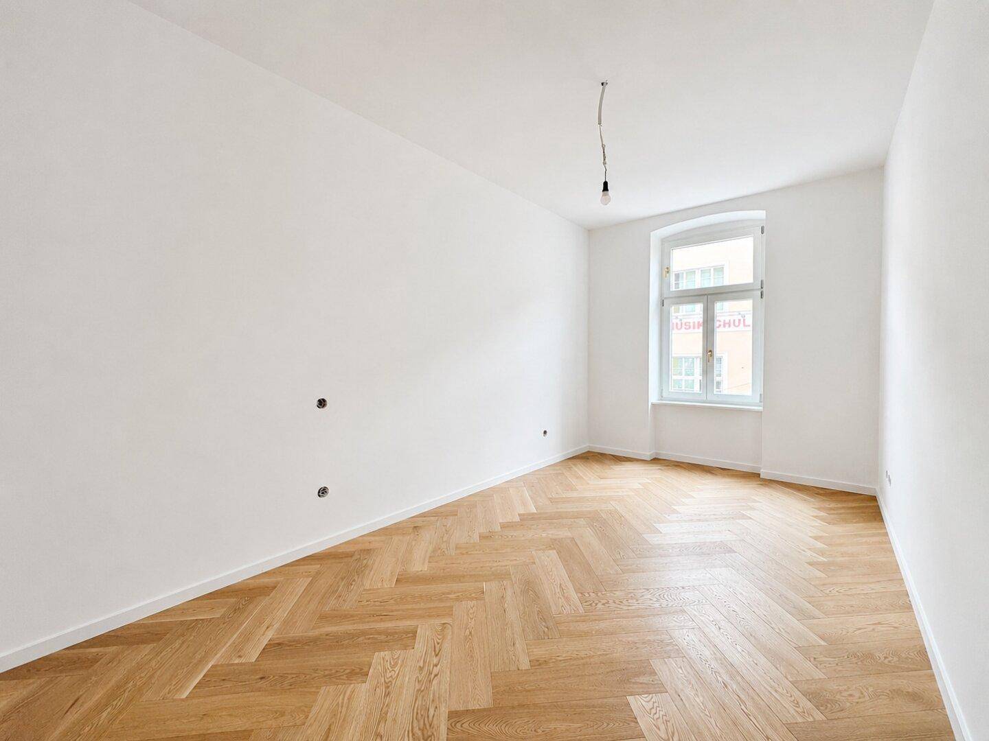 Leeres Zimmer mit hellem Fischgrätparkett und einem großen Fenster, bereit zur individuellen Gestaltung.