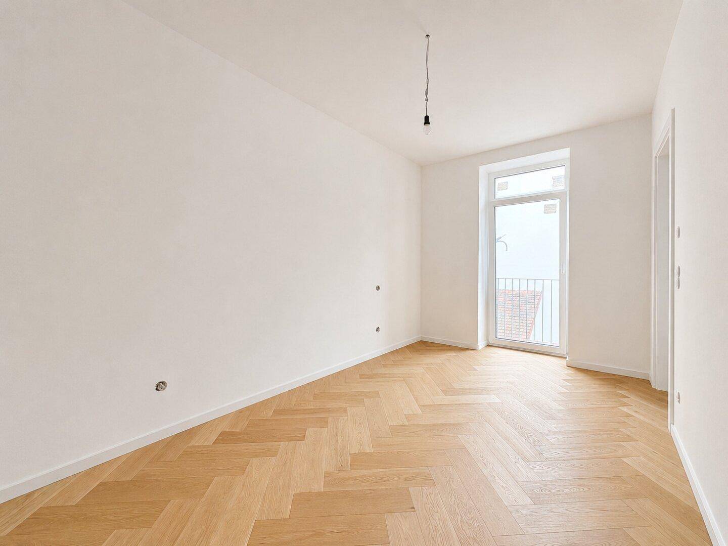 Heller Raum mit Fischgrätparkett und Zugang zu einem französischen Balkon.