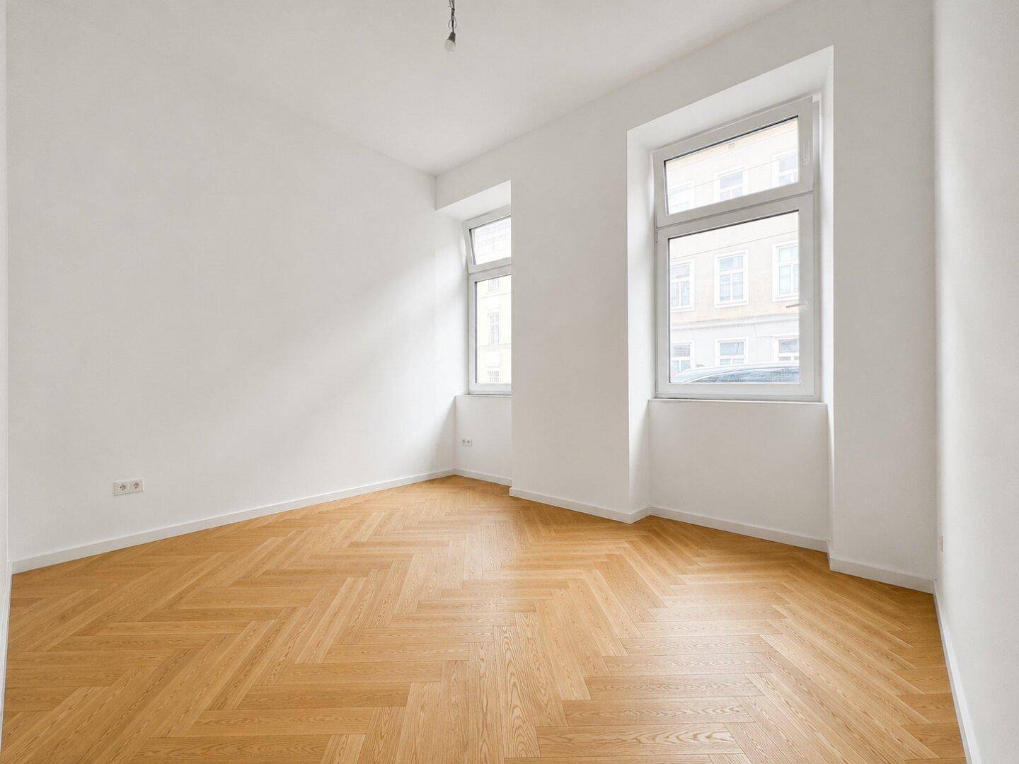 Helles Zimmer mit zwei Fenstern und Fischgrätparkett, bietet eine angenehme Wohnatmosphäre.