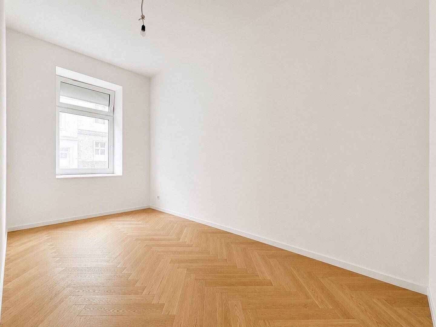 Freundliches Zimmer mit großem Fenster und Fischgrätparkett, ideal als Schlaf- oder Arbeitszimmer.