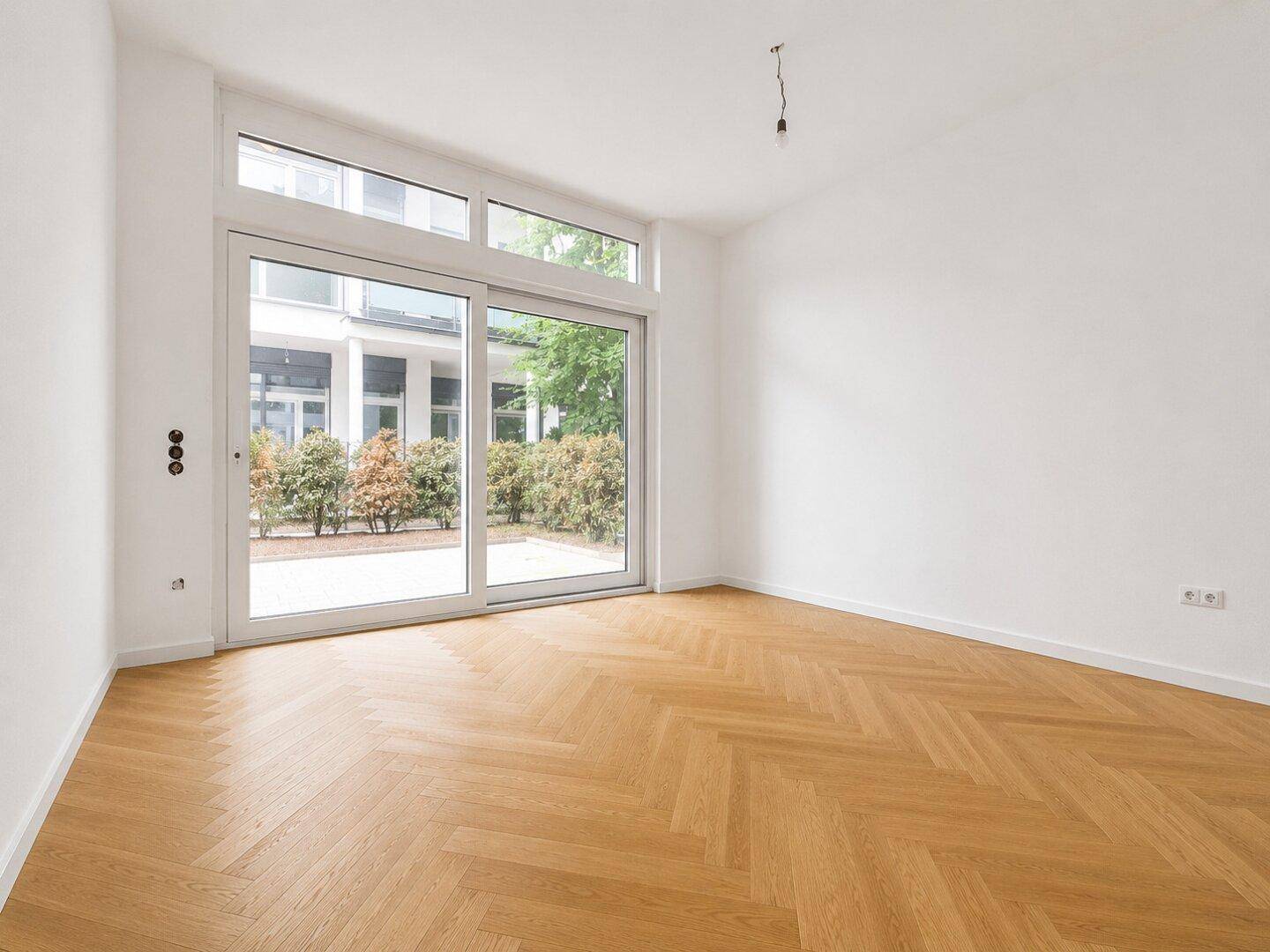 Lichtdurchfluteter Raum mit elegantem Fischgrätparkett und Schiebetüren zum Außenbereich.