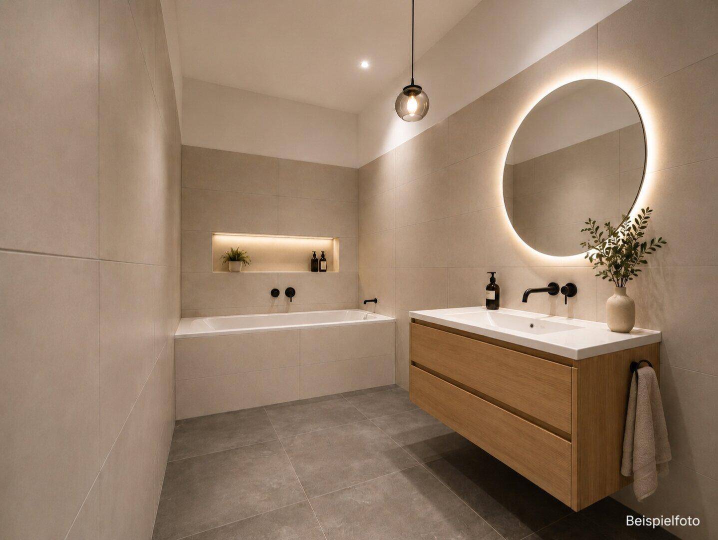 Modernes Badezimmer mit großen Fliesen, eingelassener Badewanne und beleuchtetem Spiegel.