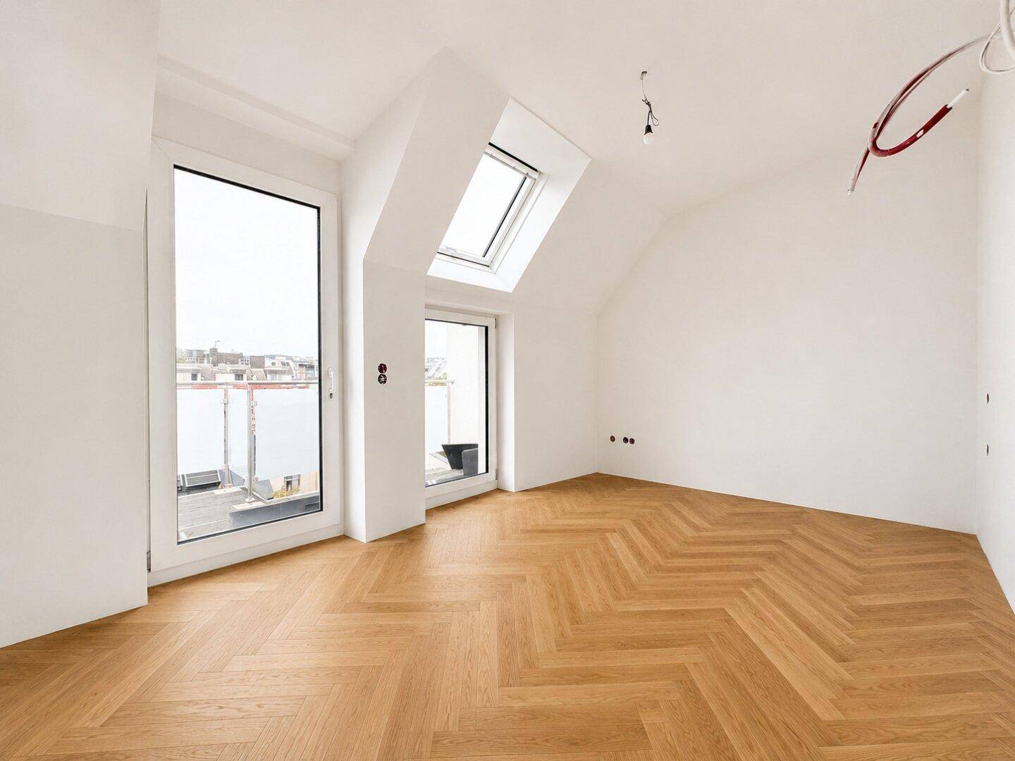 Leeres Schlafzimmer mit Fischgrätparkett, großen Fenstern, Dachfenster und Balkonzugang.
