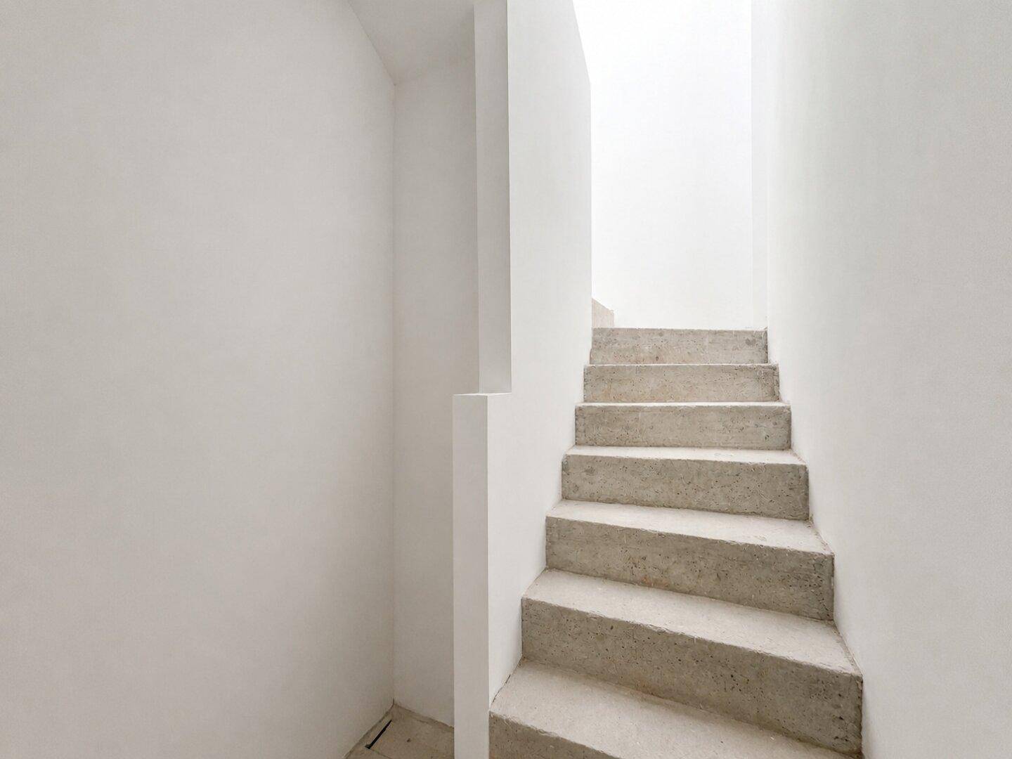 Schlichtes Treppenhaus mit Betonstufen und weißen Wänden, das die Etagen verbindet.
