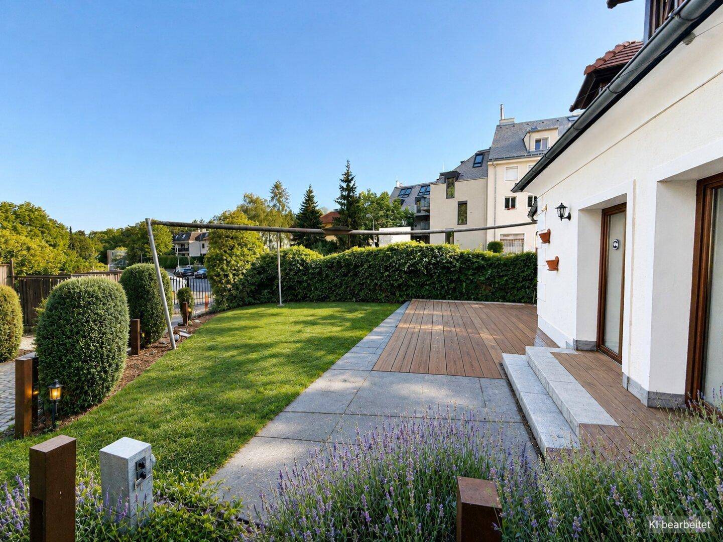 Gepflegter Garten mit Rasenfläche, Holzterrasse und blühendem Lavendel unter blauem Himmel.