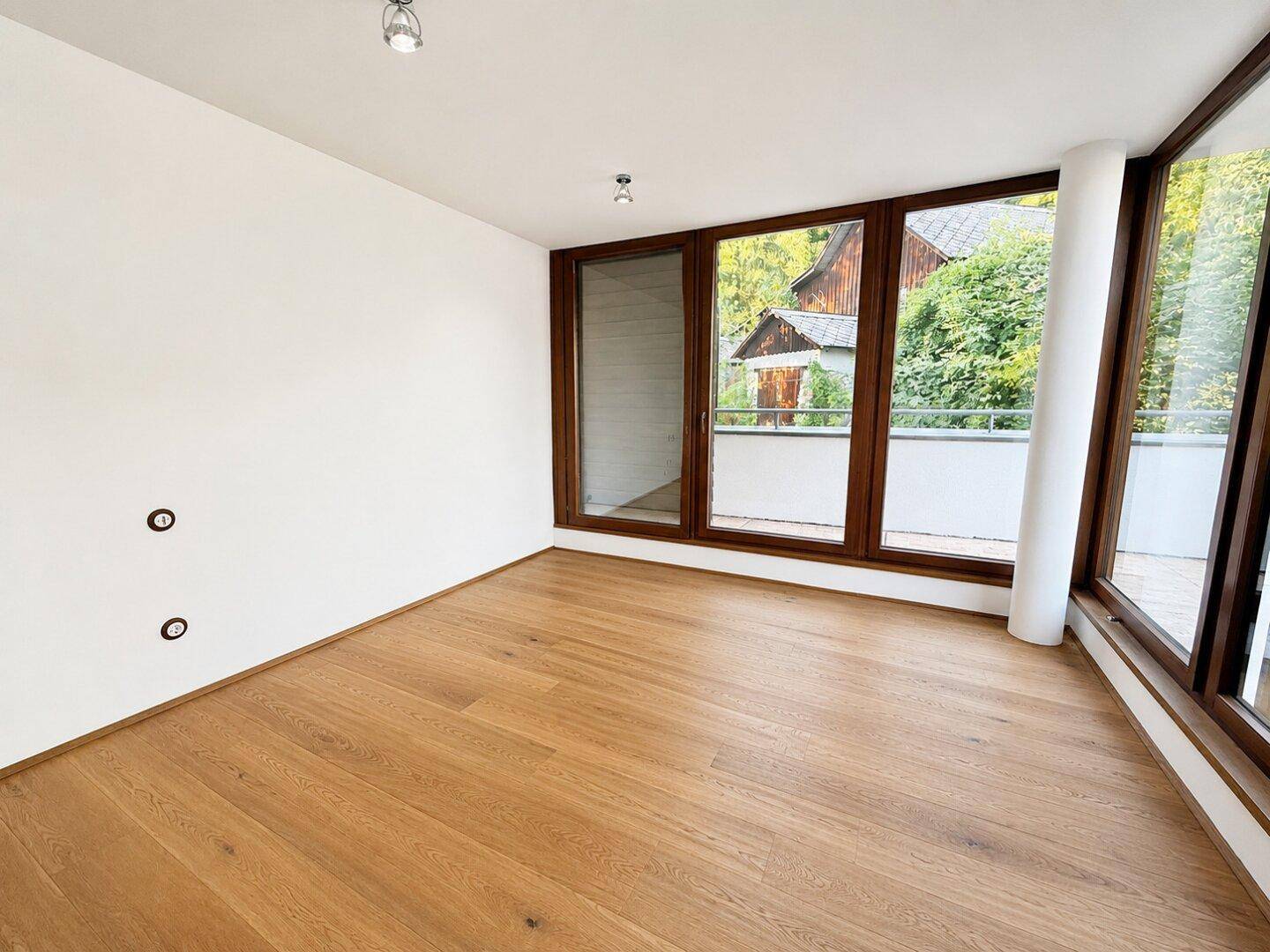 Heller Raum mit Holzboden und großen Fenstern, die viel Tageslicht hereinlassen.