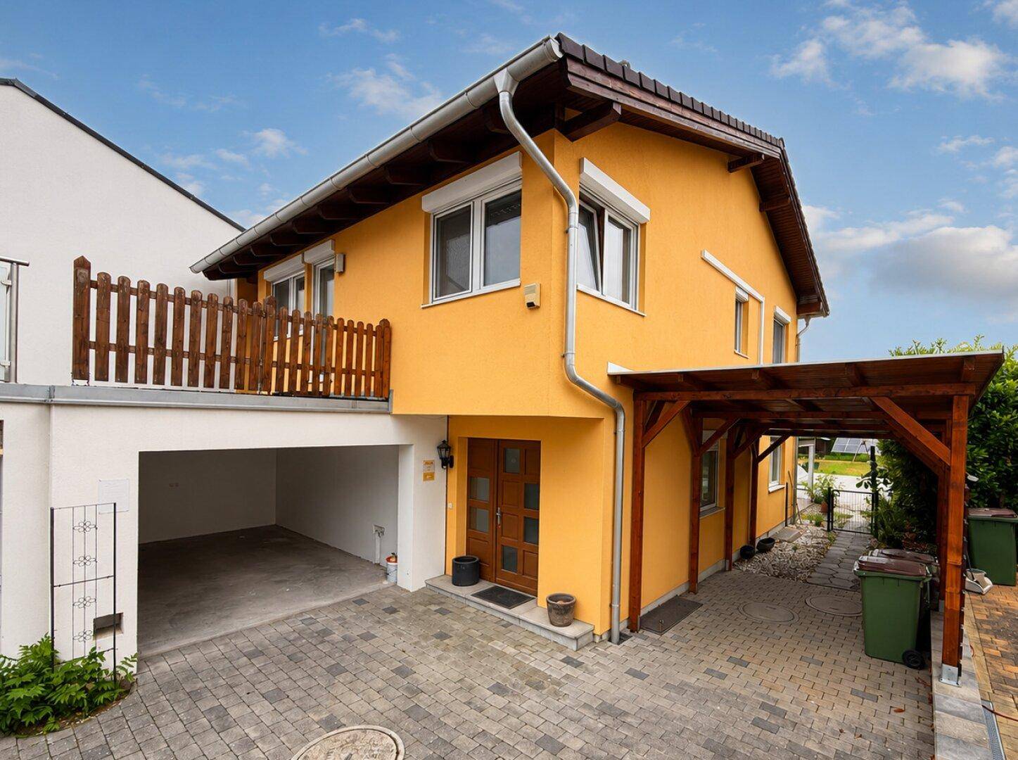 Gelbes Haus mit Eingangsbereich, Carport und integrierter Garage sowie gepflasterter Einfahrt.
