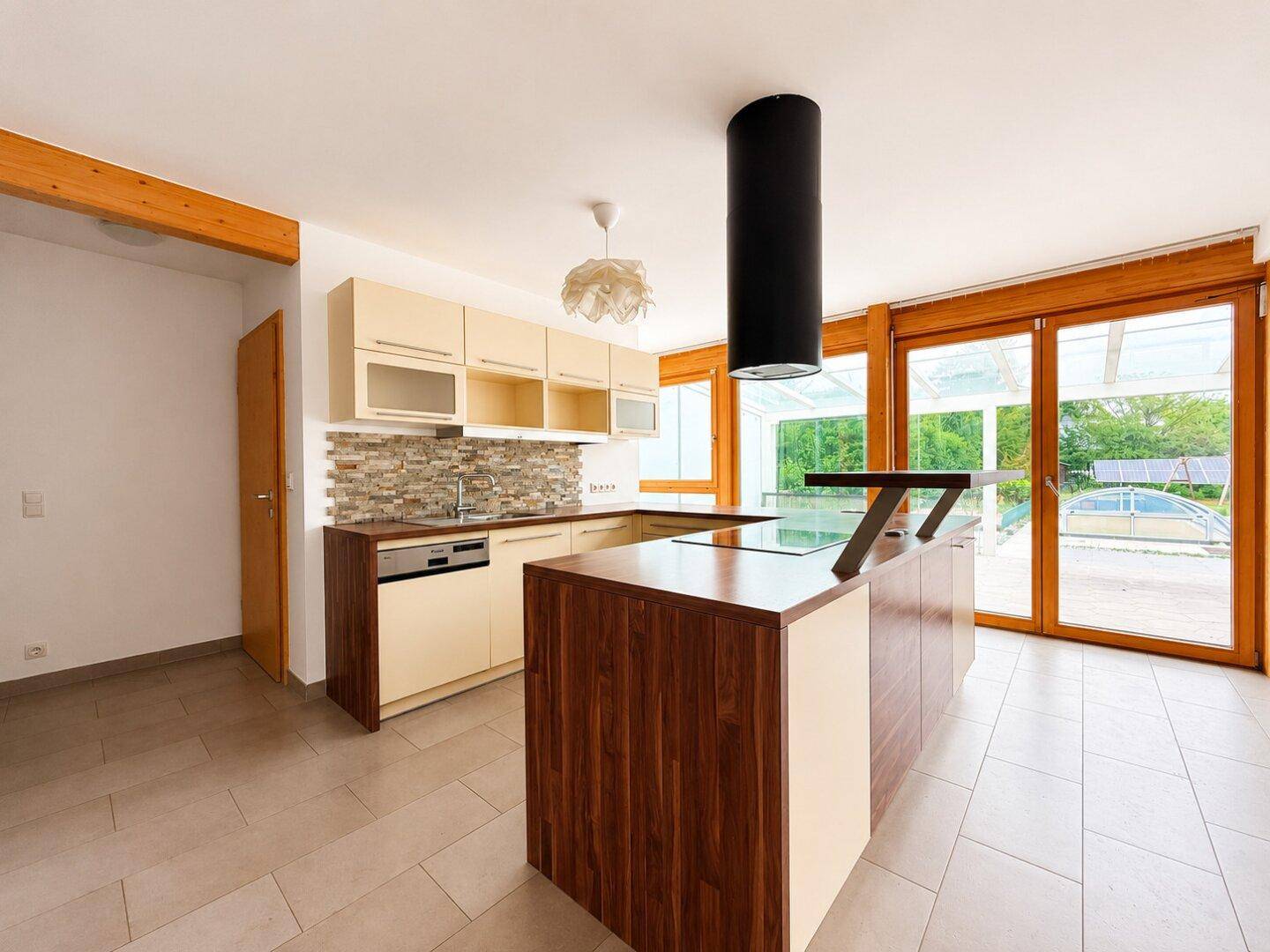 Moderne Küche mit heller Einbauküche, Kochinsel und großen Glasfronten zum Außenbereich.