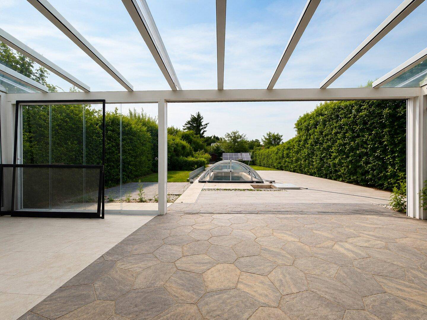 Heller Wintergarten mit Blick auf die geflieste Terrasse und den Poolbereich mit Abdeckung.