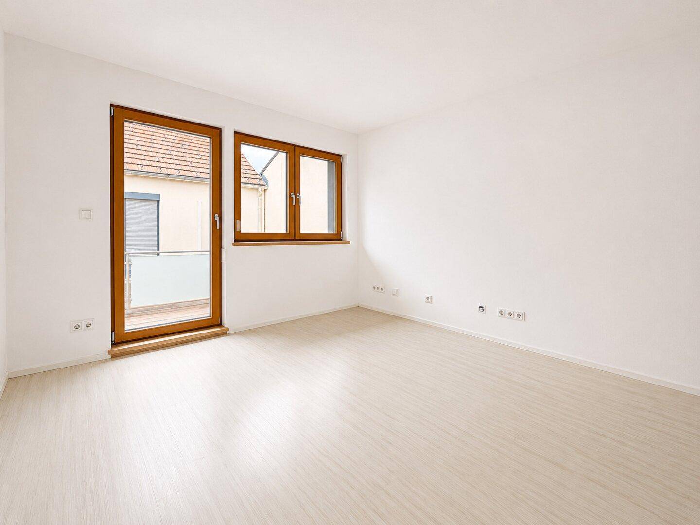 Helles Zimmer mit hellem Holzboden und Zugang zu einem kleinen Balkon.