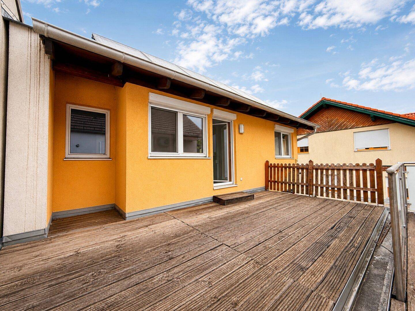 Geräumige Holzterrasse am Haus mit gelber Fassade und Solaranlage auf dem Dach.
