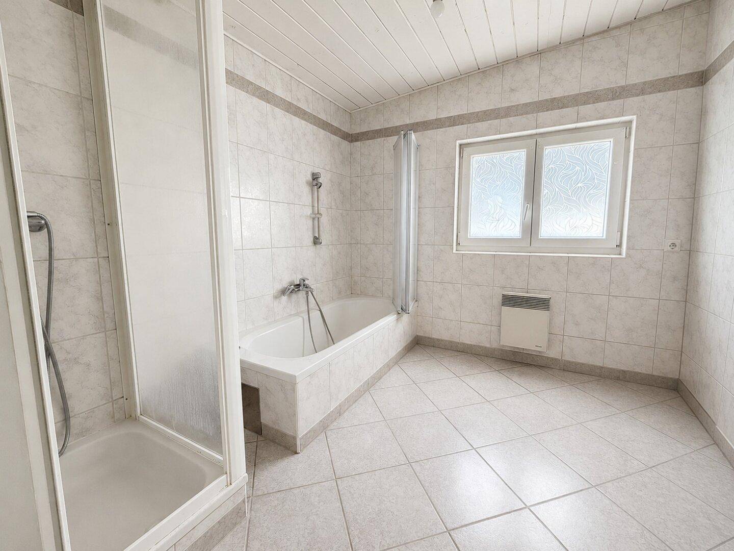 Klassisches Badezimmer mit weißen Fliesen, Badewanne, Dusche und Fenster.