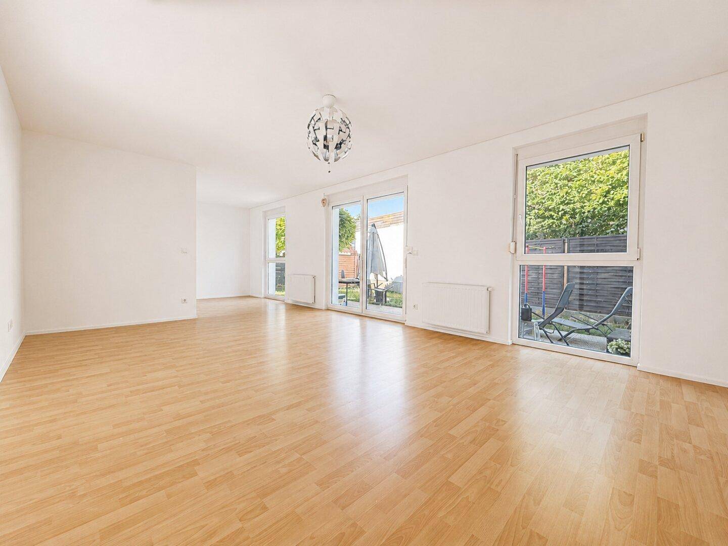 Geräumiges Wohnzimmer mit Holzboden, großen Fenstern und direktem Zugang zur Terrasse.