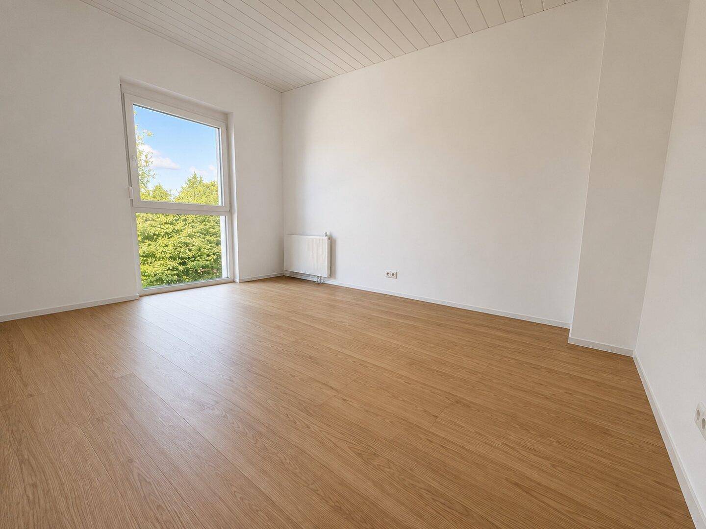 Helles Schlafzimmer mit Holzboden, großem Fenster und Ausblick ins Grüne.