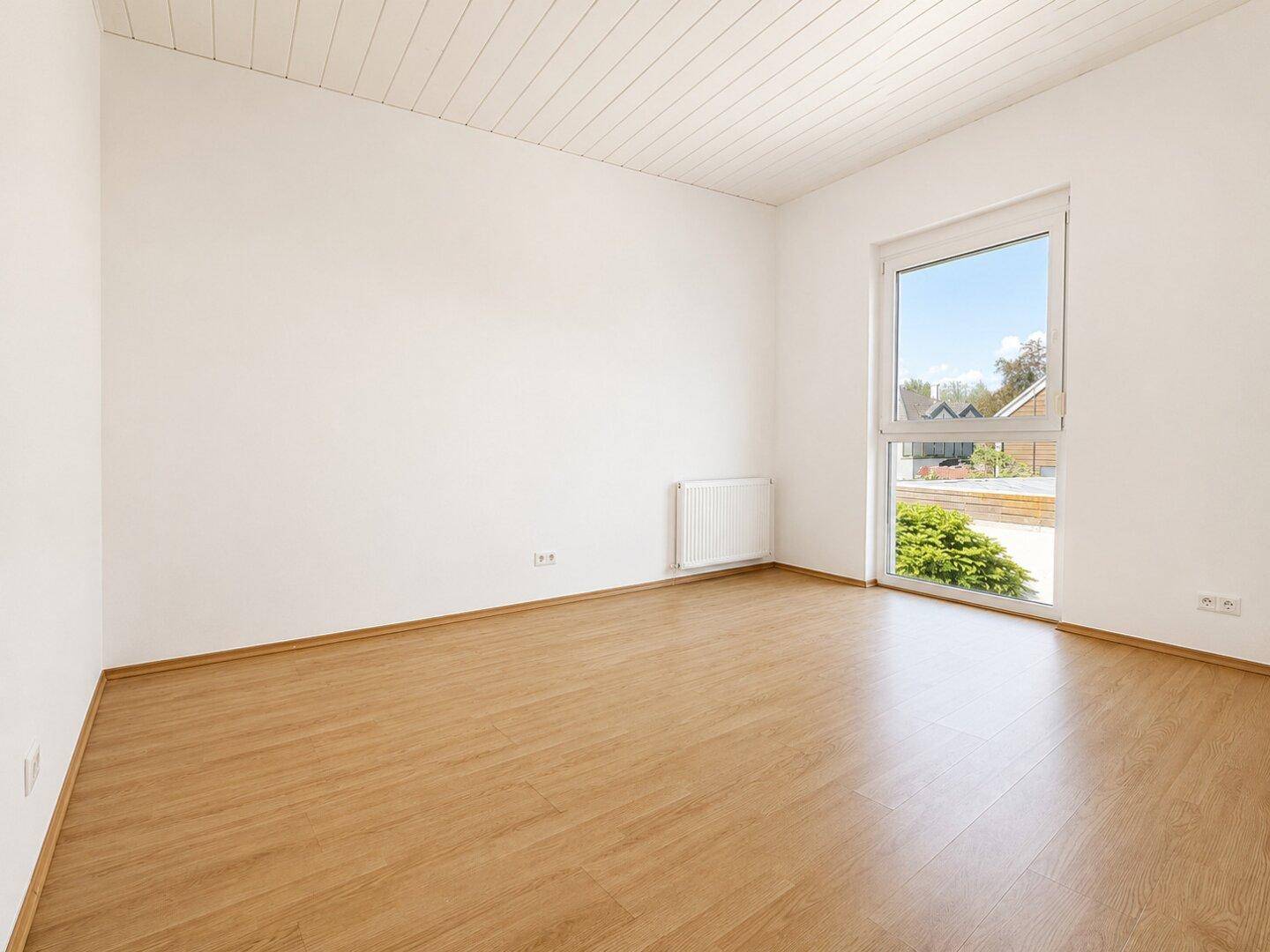 Leerer Raum mit Holzboden und Eckfenster, das viel Licht spendet.