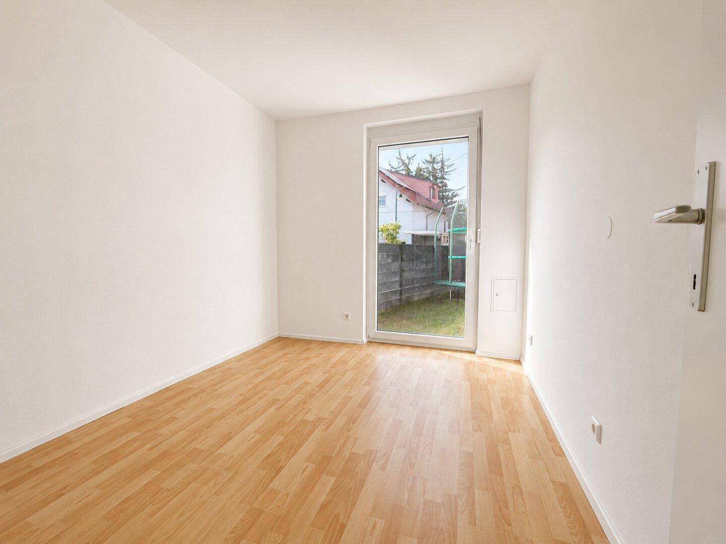 Leerer Raum mit Holzboden und Fenster, das viel Tageslicht hereinlässt.