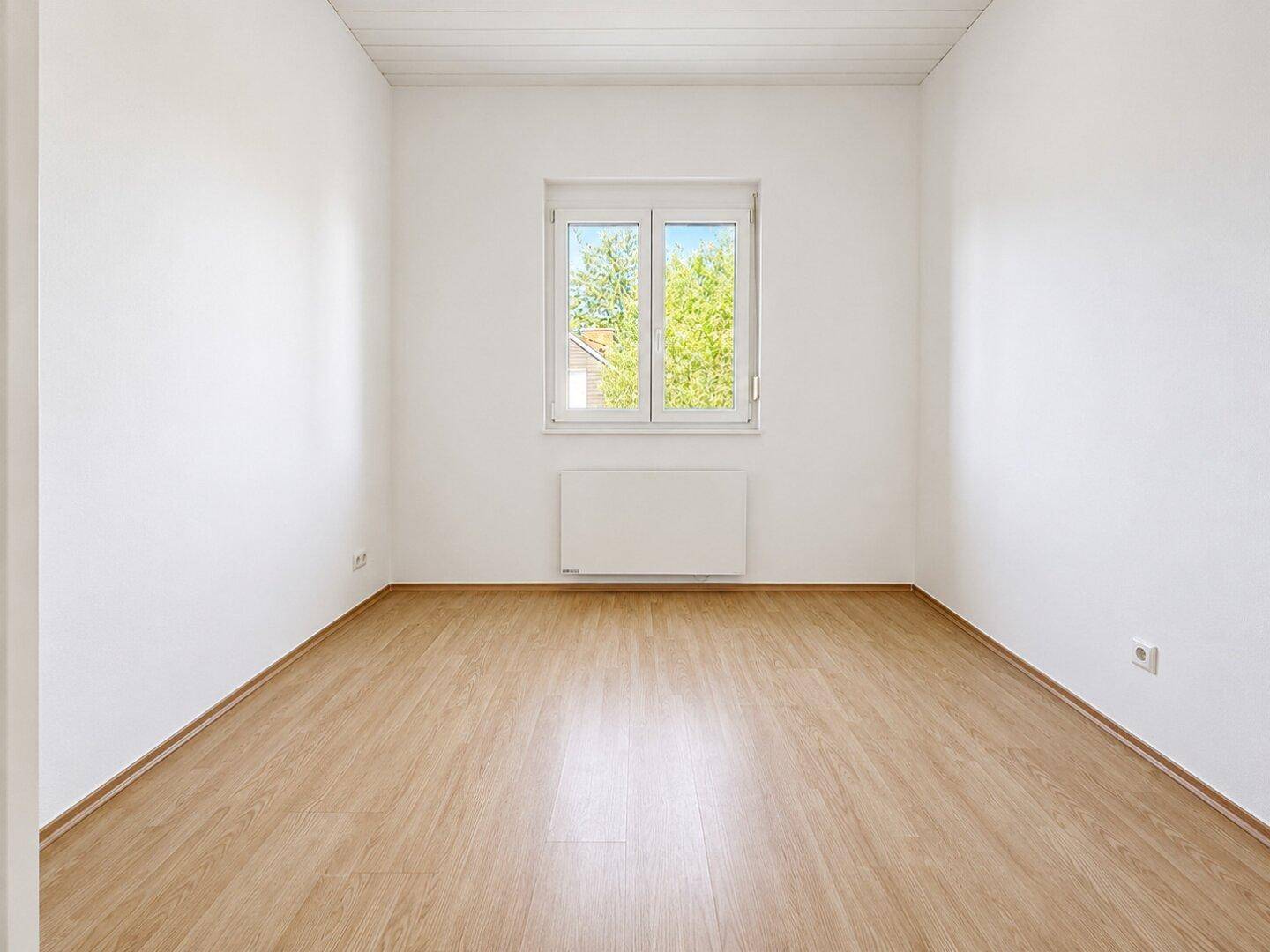 Heller Raum mit Holzboden und einem Fenster, das für gute Belichtung sorgt.