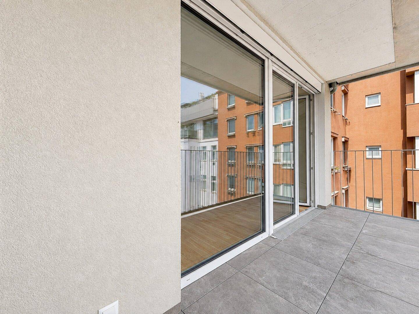Balkon mit grauen Fliesen und Blick auf die umliegenden Gebäude der Nachbarschaft.