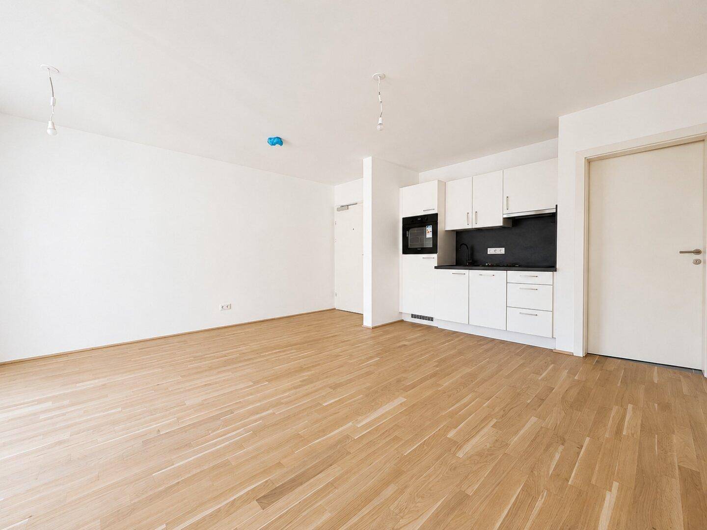 Heller Raum mit Parkettboden und einer kompakten, modernen Küchenzeile an der Wand.