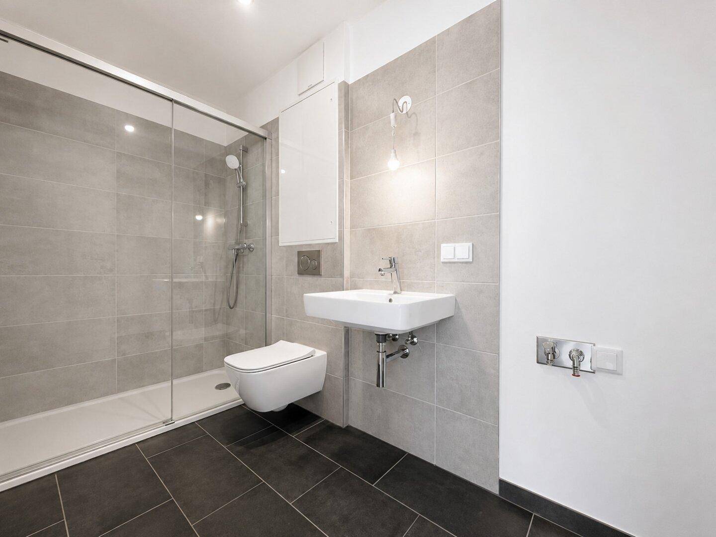 Modernes Badezimmer mit begehbarer Dusche, Wand-WC und grauen Fliesen.