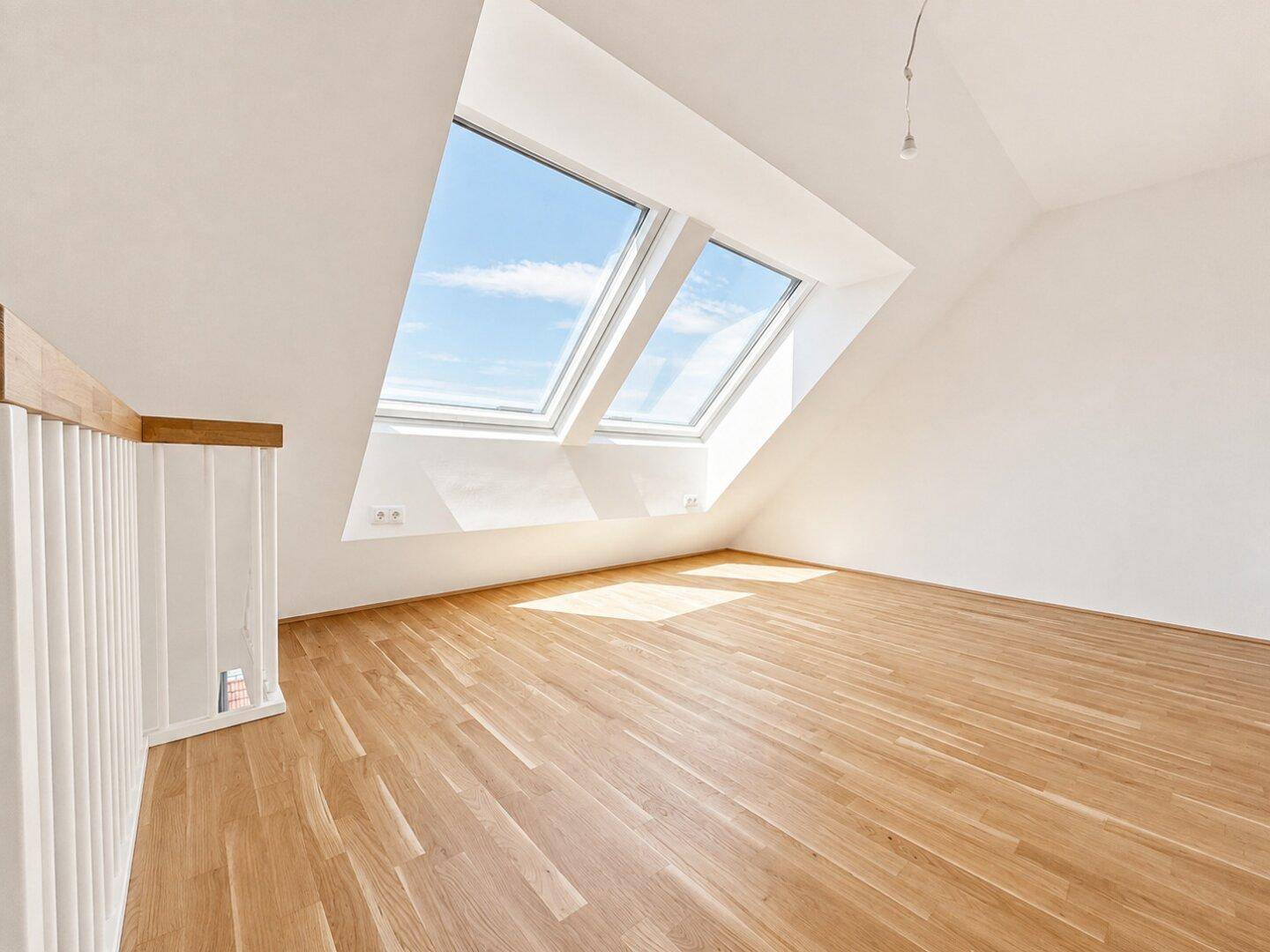Lichtdurchfluteter Dachgeschossraum mit Holzboden und zwei großen Dachfenstern.