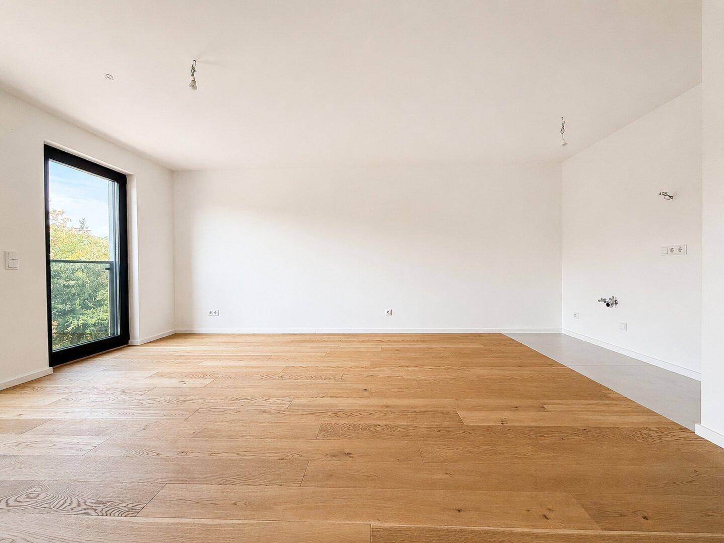 Heller, leerer Raum mit Eichenparkettboden und großer Fensterfront zum Außenbereich.