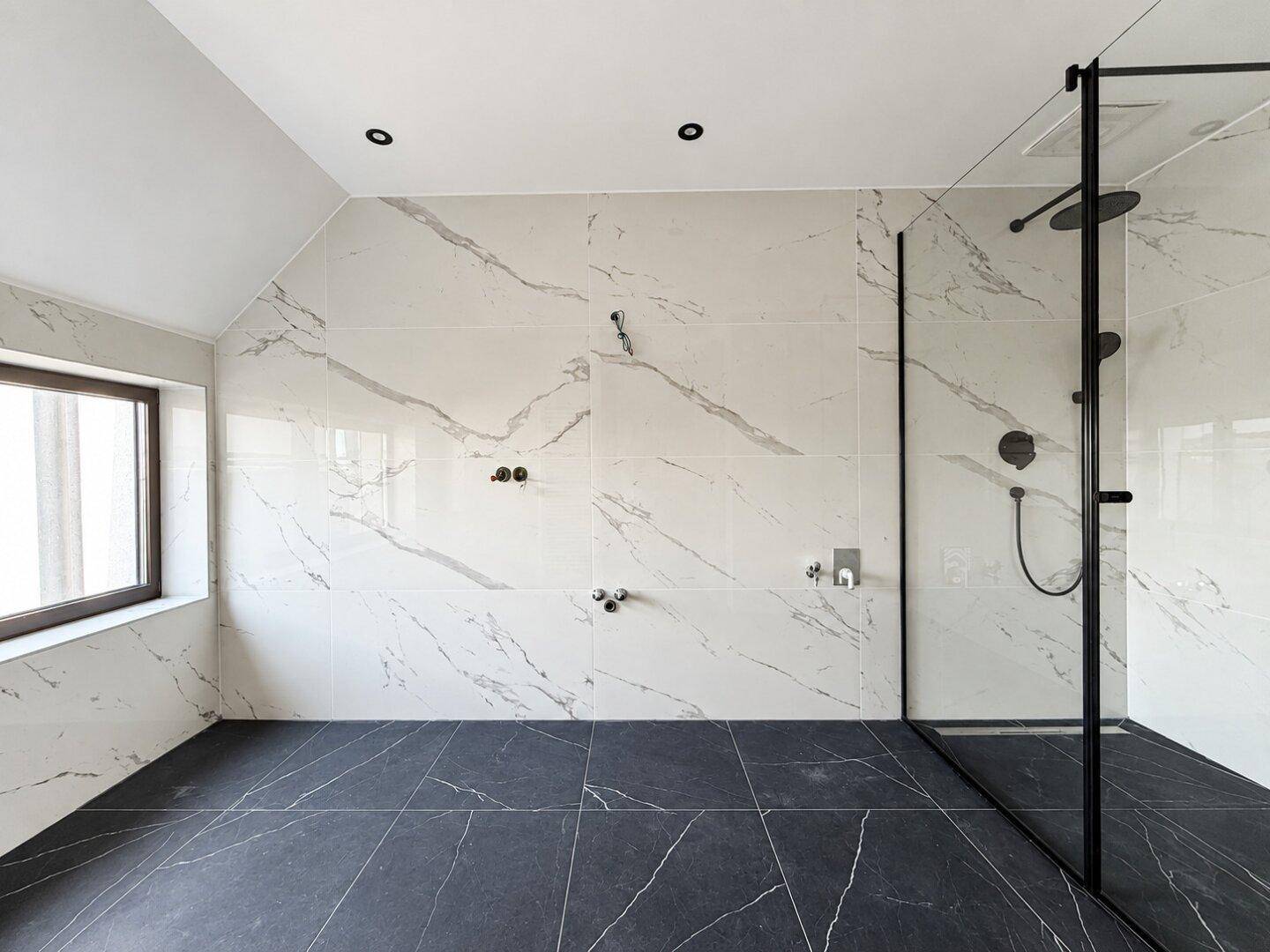 Modernes Badezimmer mit großformatigen Marmorfliesen, begehbarer Dusche und Dachschräge.
